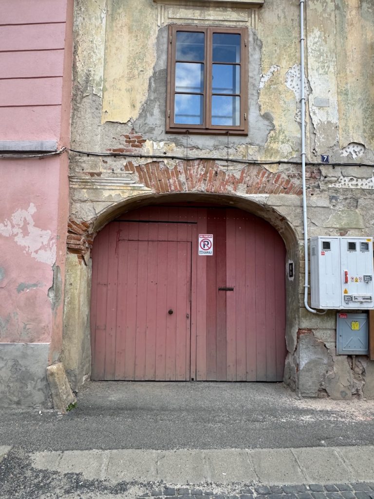 weinrotes Hoftor in Hermannstadt an stark beschädigter Hauswand