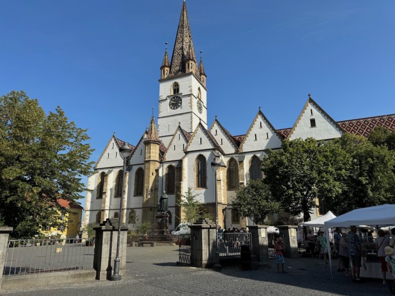 Evangelische Stadtpfarrkirche in Hermannstadt (Sibiu) an einem sonnigen Tag – gotische Architektur mit spitzem Turm, Marktstände und Besucher im Vordergrund.