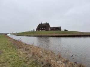 Warft mit reetgedecktem Haus auf Hallig Hooge im Winter, umgeben von Wasser und Deichlandschaft.