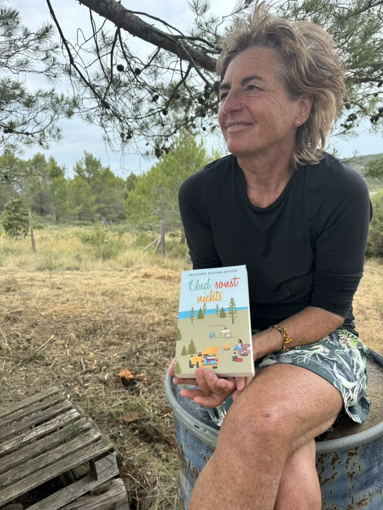 Autorin Irmgard Rosina Bauer sitzt in der Natur und hält ihr Buch „Und sonst nichts“ in der Hand – ein Moment der Ruhe und Reflexion während einer Reise.