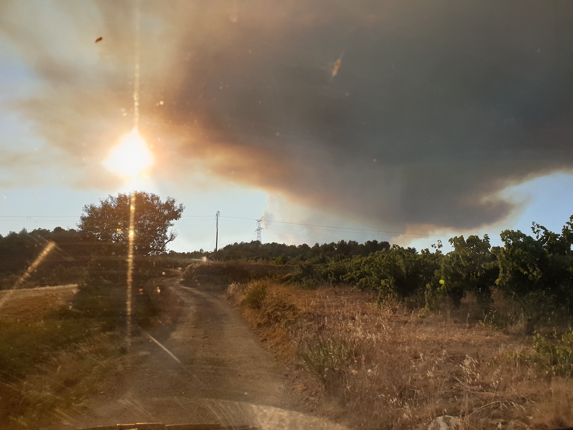 Staubiger Weg in der Natur mit tiefstehender Sonne und bedrohlichen Rauchwolken am Himmel