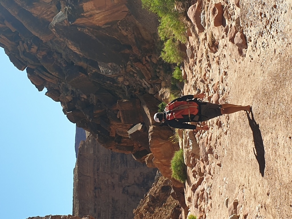 Wanderer mit Rucksack auf einem felsigen Weg durch einen roten Canyon. Das Bild symbolisiert Umwege, Orientierung und die Erkenntnis, dass Verirren manchmal zu den schönsten Erfahrungen einer Reise gehört.