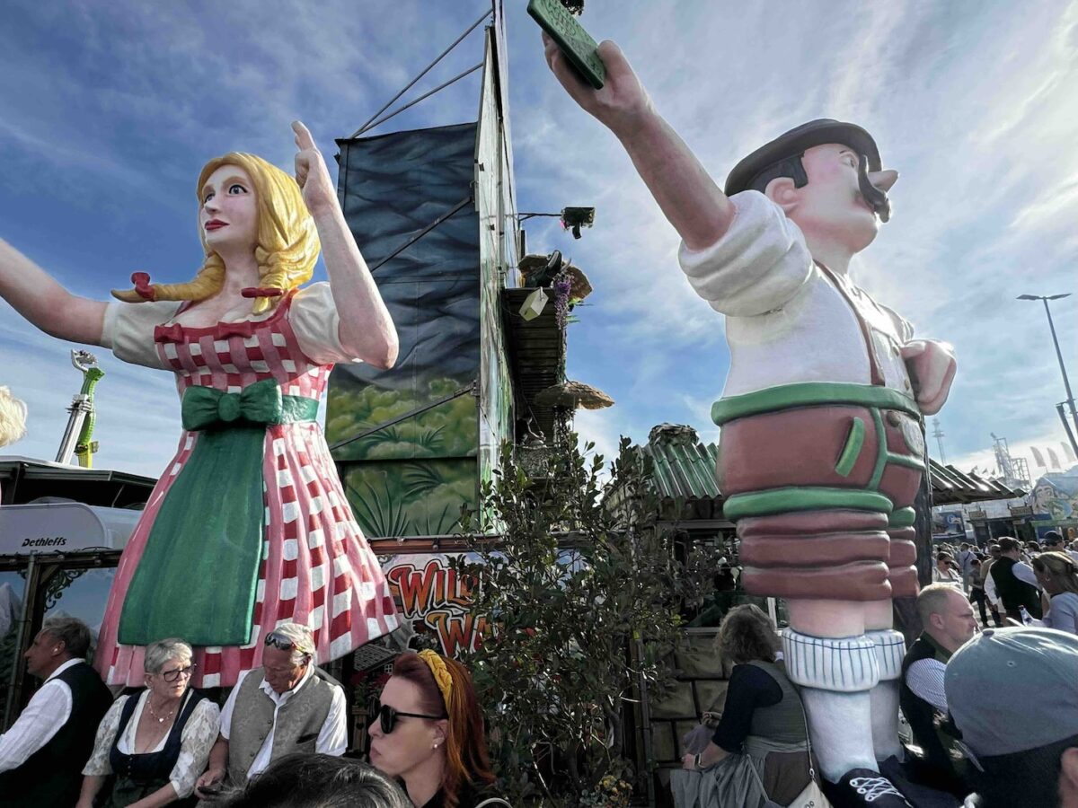 Große bunte Figuren einer Frau im Dirndl und eines Mannes in Lederhose auf dem Oktoberfest in München.